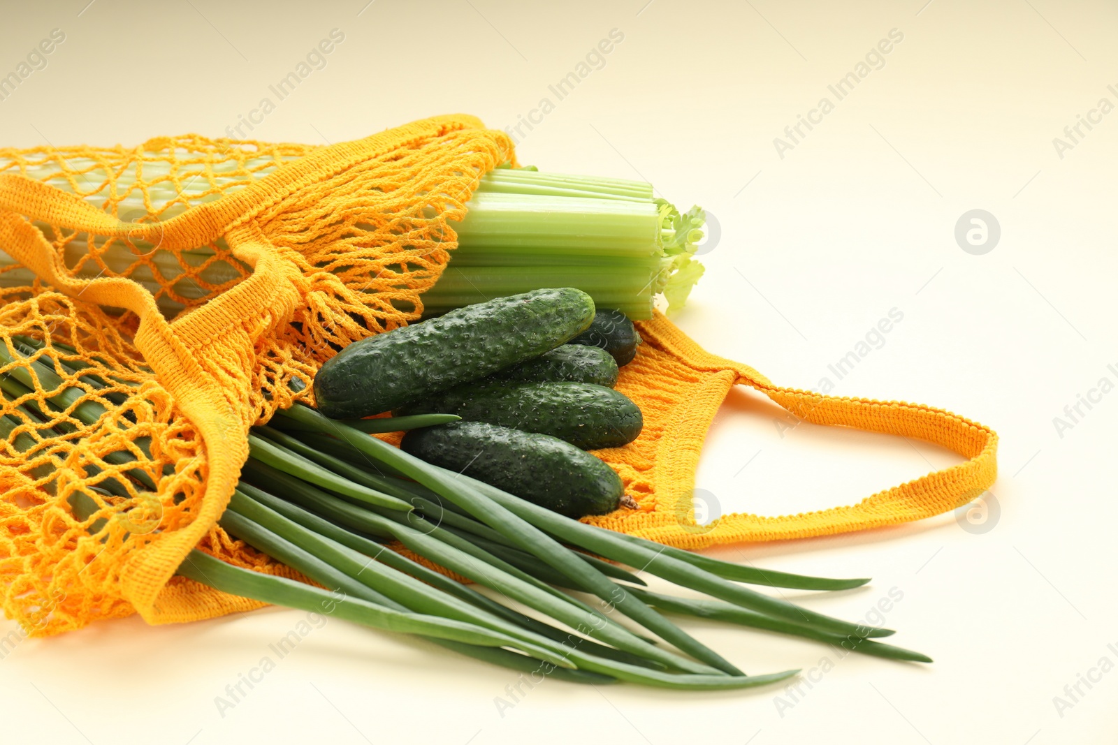 Photo of String bag with different vegetables on beige background, closeup