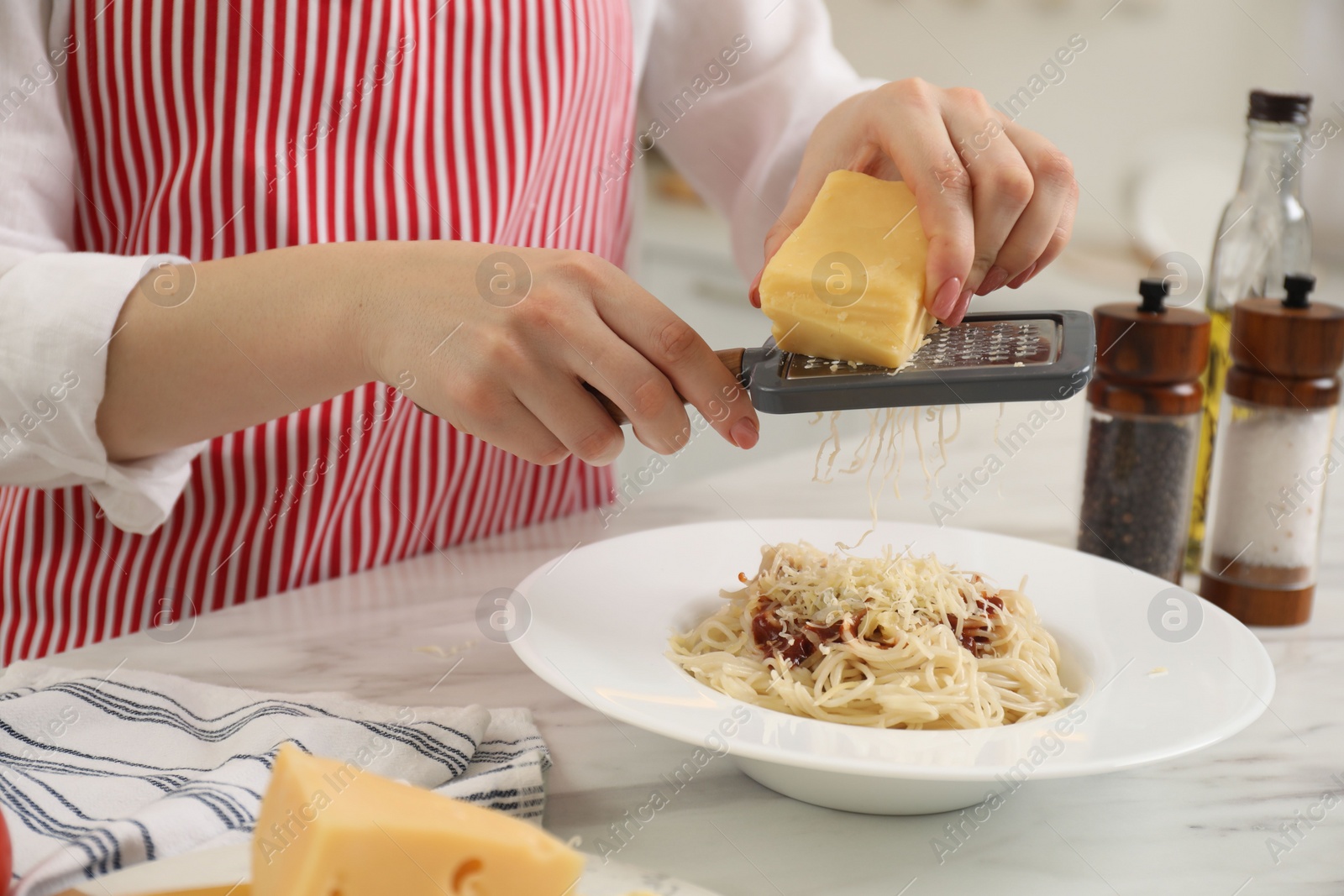 Photo of Woman grating cheese onto delicious pasta at white marble table in kitchen, closeup