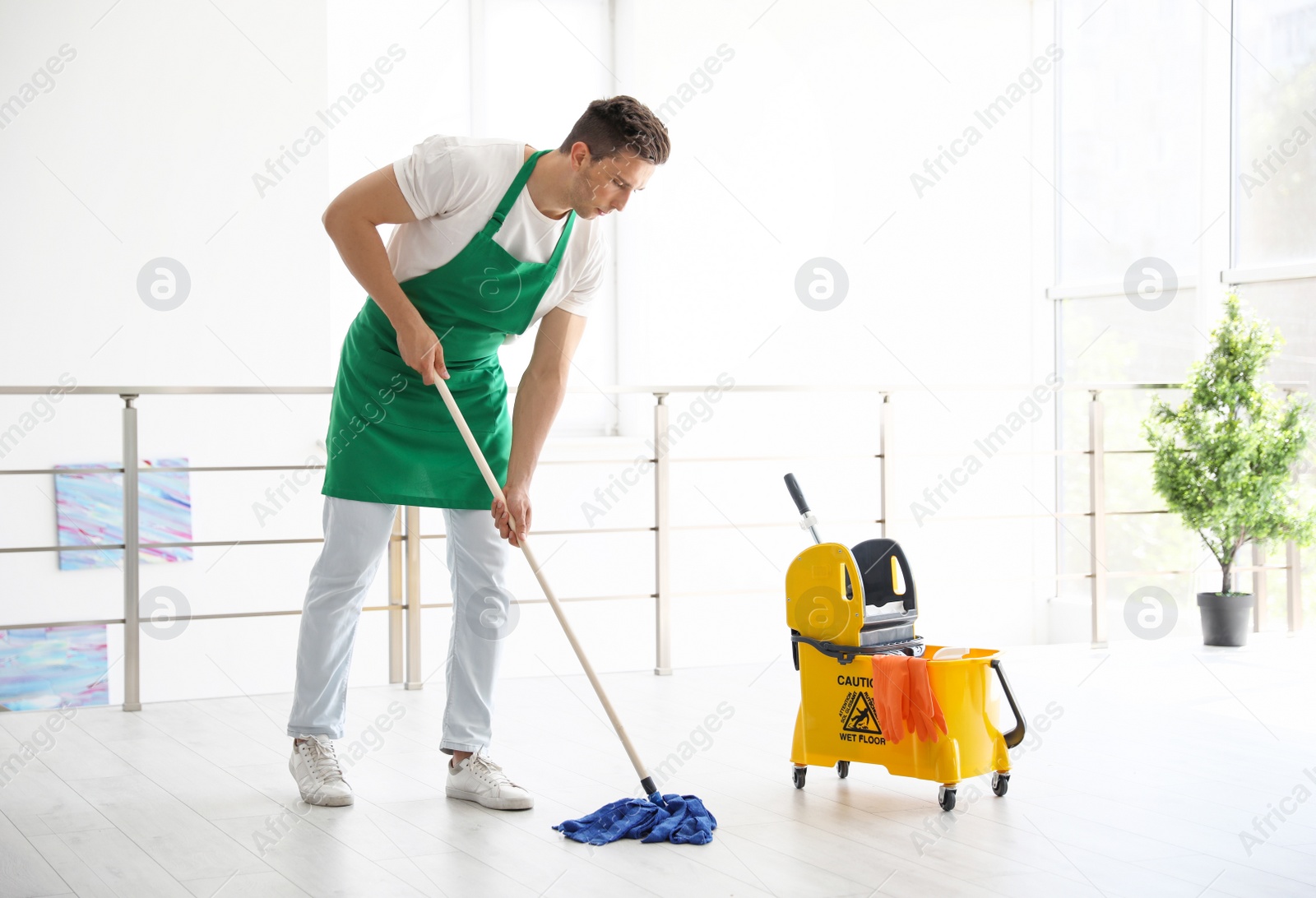 Photo of Young man with mop cleaning floor, indoors