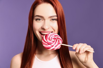 Woman with red dyed hair biting lollipop on purple background