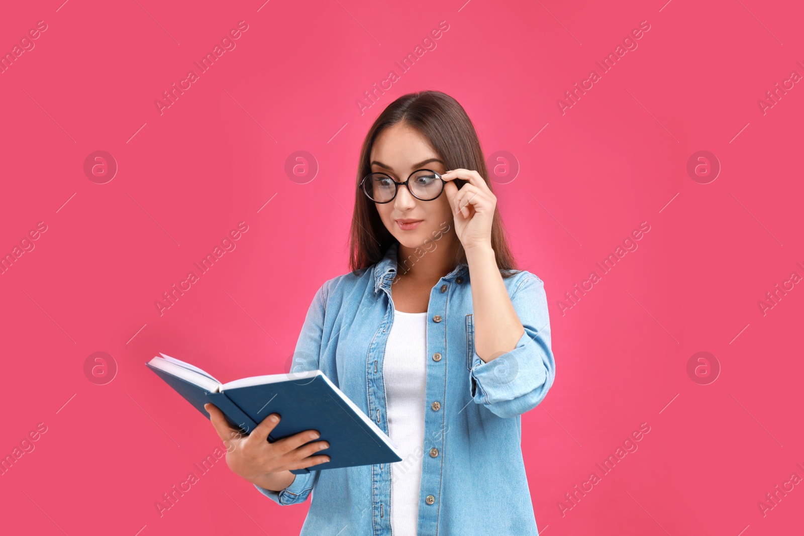 Photo of Beautiful young woman with glasses and book on crimson background