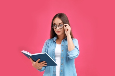 Photo of Beautiful young woman with glasses and book on crimson background