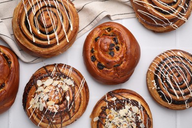 Delicious rolls with raisins, nuts and toppings on white tiled table, flat lay. Sweet buns