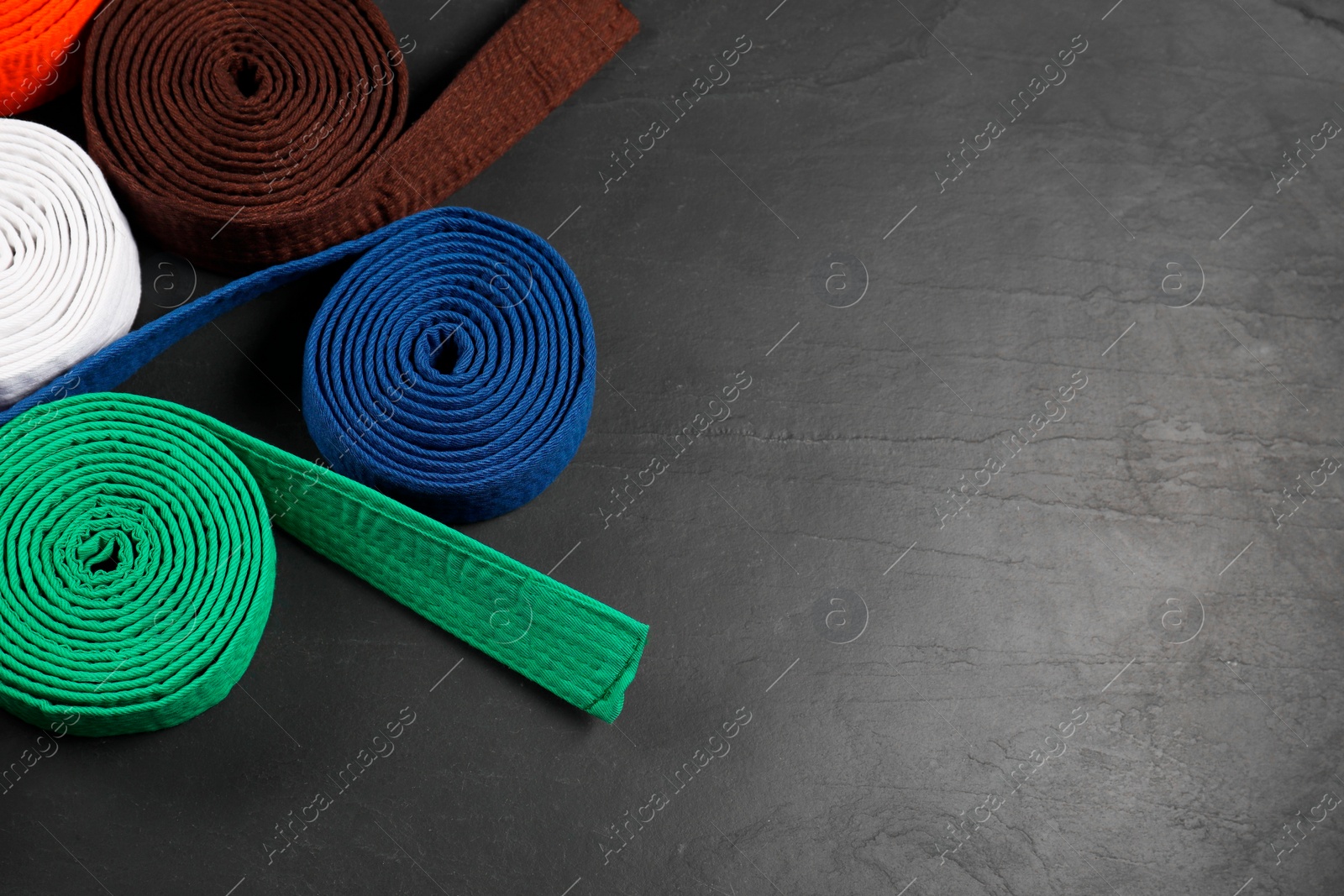 Photo of Colorful karate belts on gray background, flat lay. Space for text