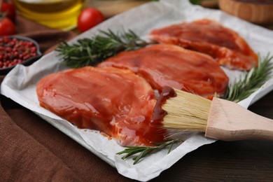 Raw marinated meat, rosemary and basting brush on table, closeup