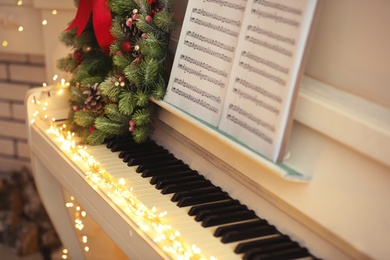 Photo of White piano with decorative wreath and note sheets closeup. Christmas music