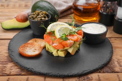 Photo of Delicious salmon tartare served with avocado, sauce and croutons on wooden table, closeup