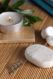 Acupuncture needles, spa stones and burning candle on bamboo mat