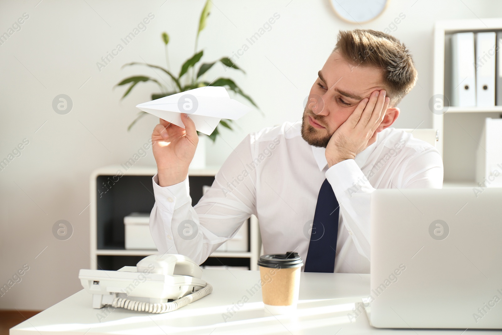 Photo of Lazy young man playing with paper plane at workplace