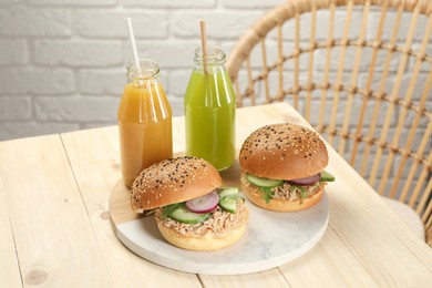 Photo of Delicious sandwiches with tuna, vegetables and bottles of juice on white wooden table indoors