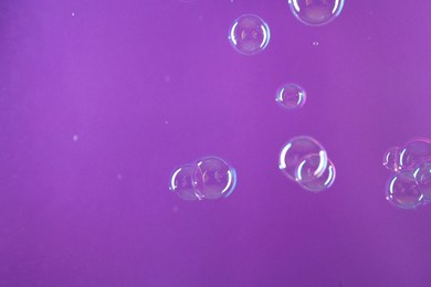 Photo of Beautiful transparent soap bubbles on violet background, space for text