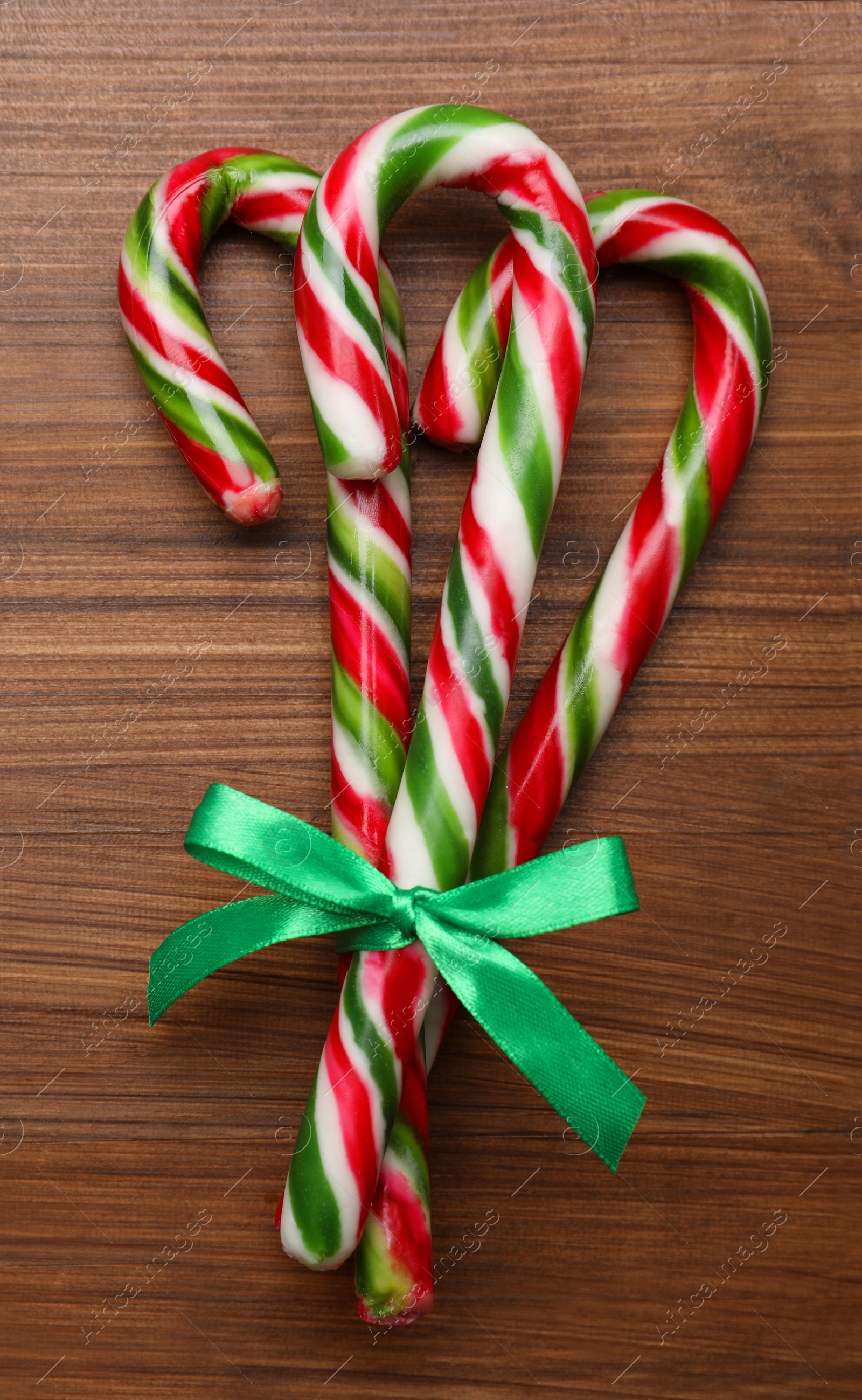 Photo of Bunch of sweet Christmas candy canes with bow on wooden table, top view