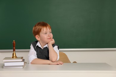 Photo of Cute little boy with books and school bell in classroom, space for text