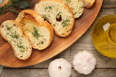 Tasty baguette with garlic, dill and oil on wooden table, flat lay
