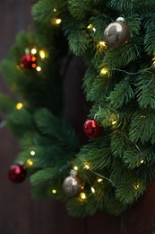 Photo of Beautiful Christmas wreath with baubles and string lights hanging on wall, closeup