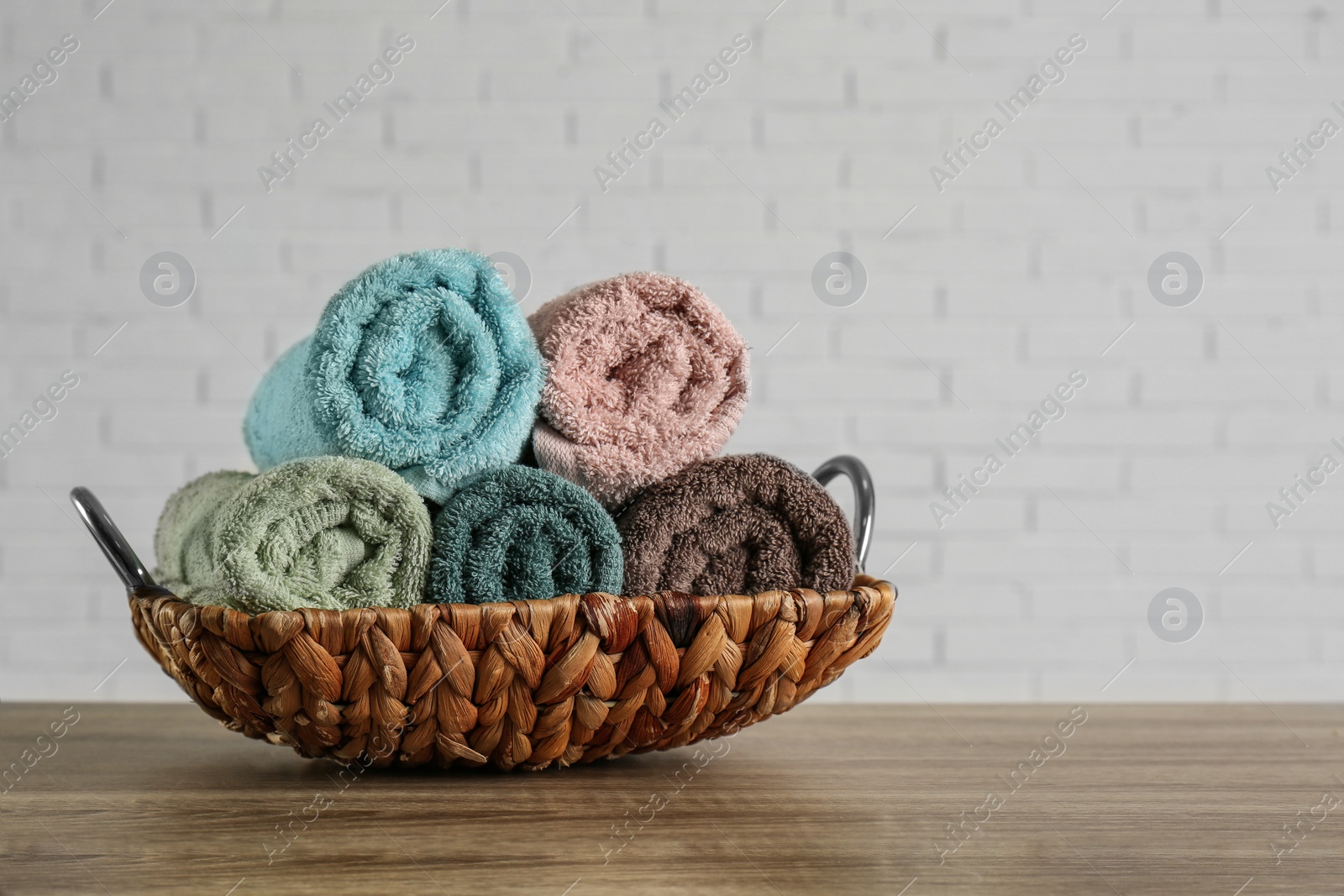 Photo of Wicker basket with rolled bath towels on wooden table near white brick wall. Space for text