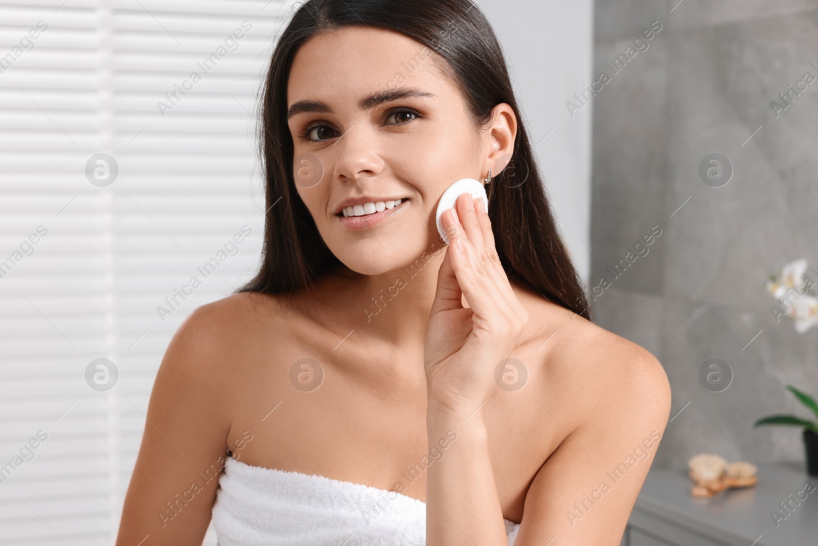 Photo of Young woman cleaning her face with cotton pad in bathroom