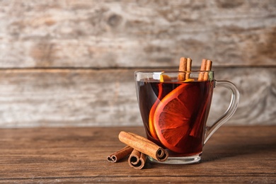 Photo of Cup of red mulled wine on table against wooden background. Space for text