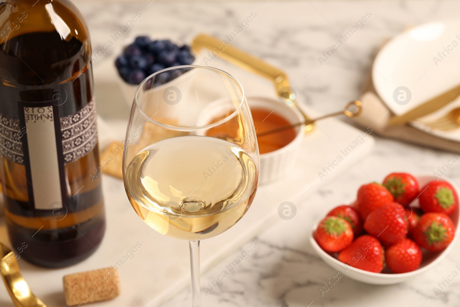 Photo of Glass of wine near bottle and delicious snacks on white table, closeup