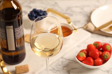 Photo of Glass of wine near bottle and delicious snacks on white table, closeup