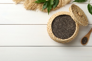 Photo of Wicker box and spoon with chia seeds on white wooden table, flat lay. Space for text