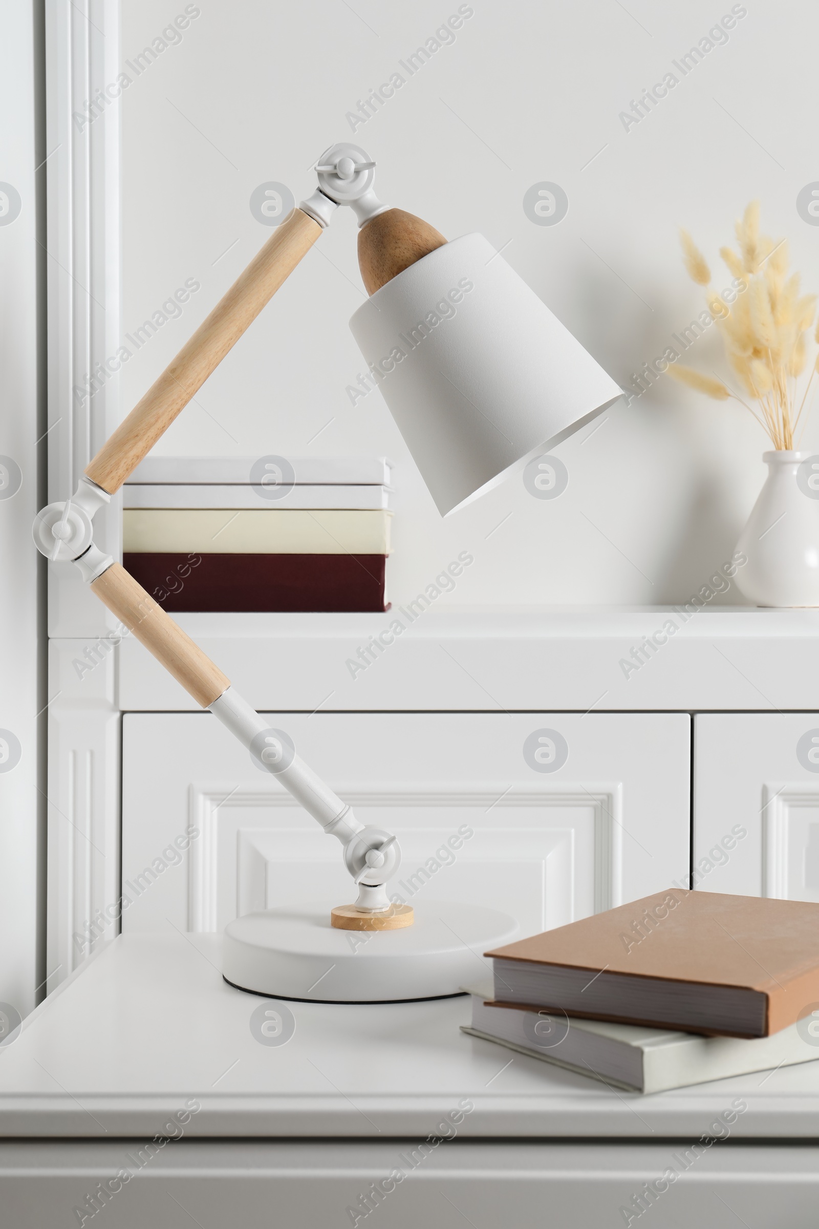 Photo of Stylish lamp and books on white side table in light room. Interior design