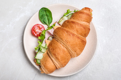 Photo of Tasty croissant sandwich with ham and cucumber on light grey marble table, top view