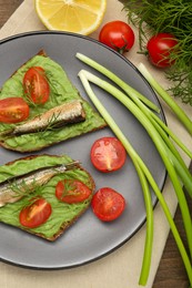 Photo of Delicious sandwiches with sprats, tomatoes, avocado puree and dill on wooden table, flat lay
