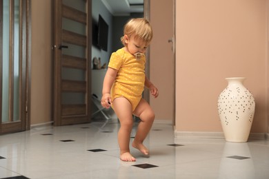 Photo of Cute baby with pacifier learning to walk in room