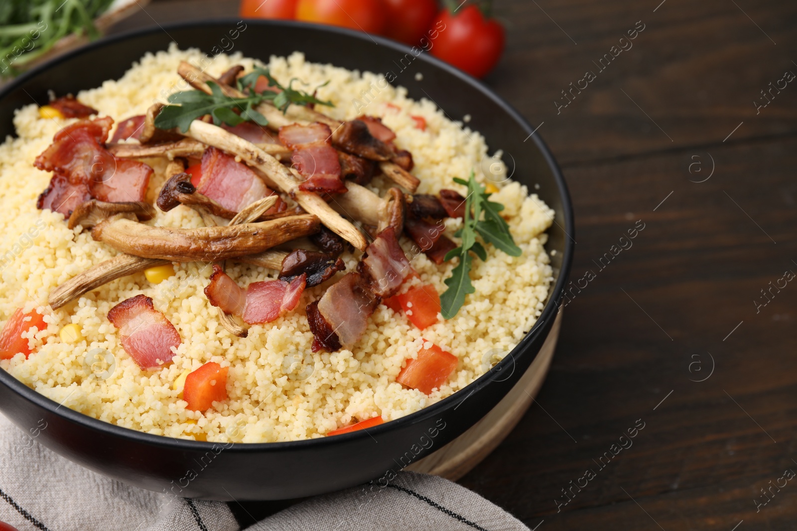 Photo of Tasty couscous with mushrooms and bacon in bowl on wooden table, closeup. Space for text