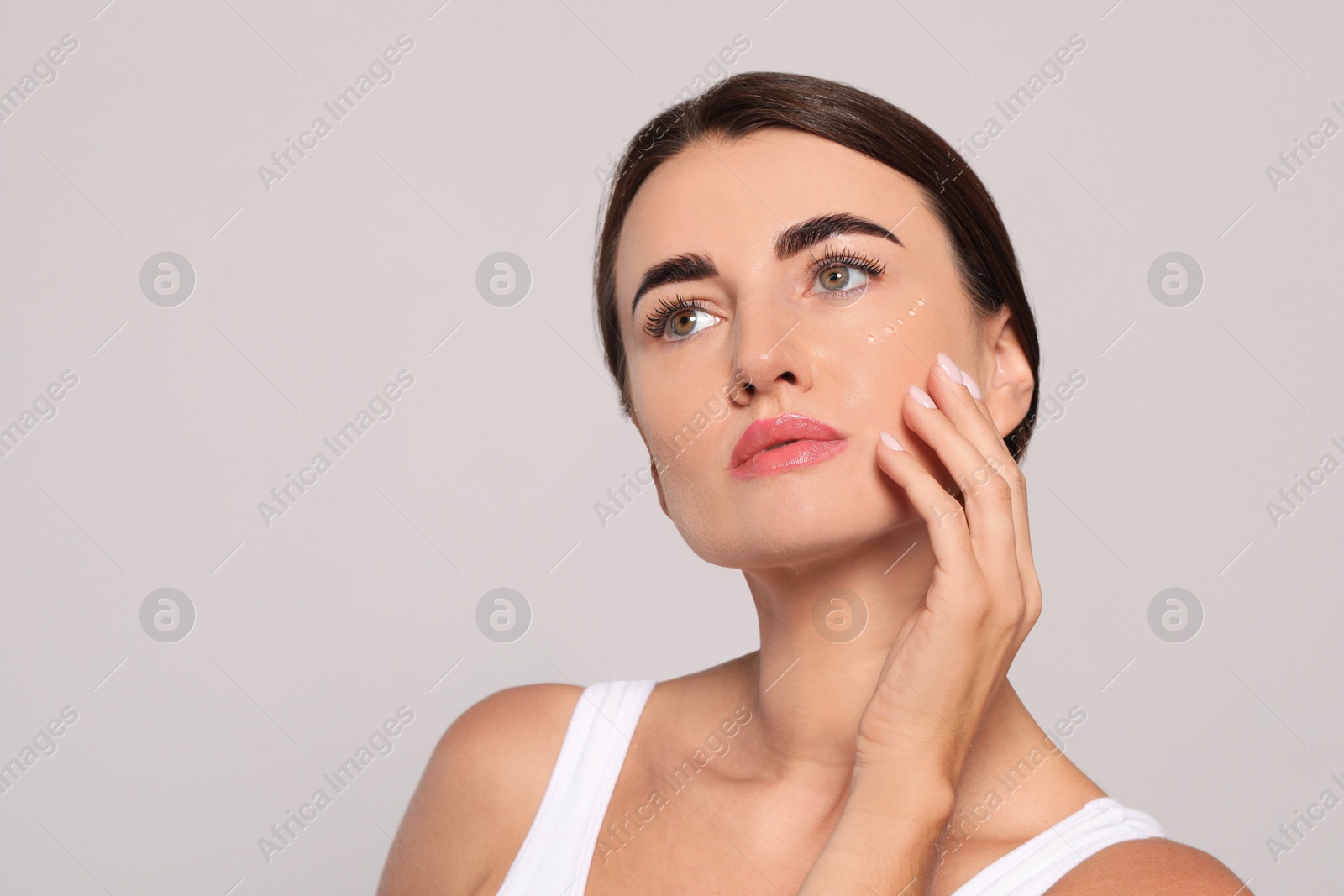 Photo of Woman with cosmetic product around eye on light background. Space for text
