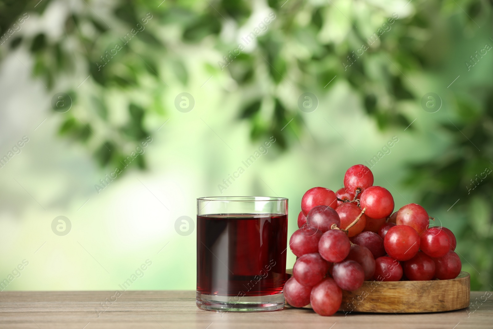 Photo of Glass of juice and fresh grapes on wooden table outdoors. Space for text