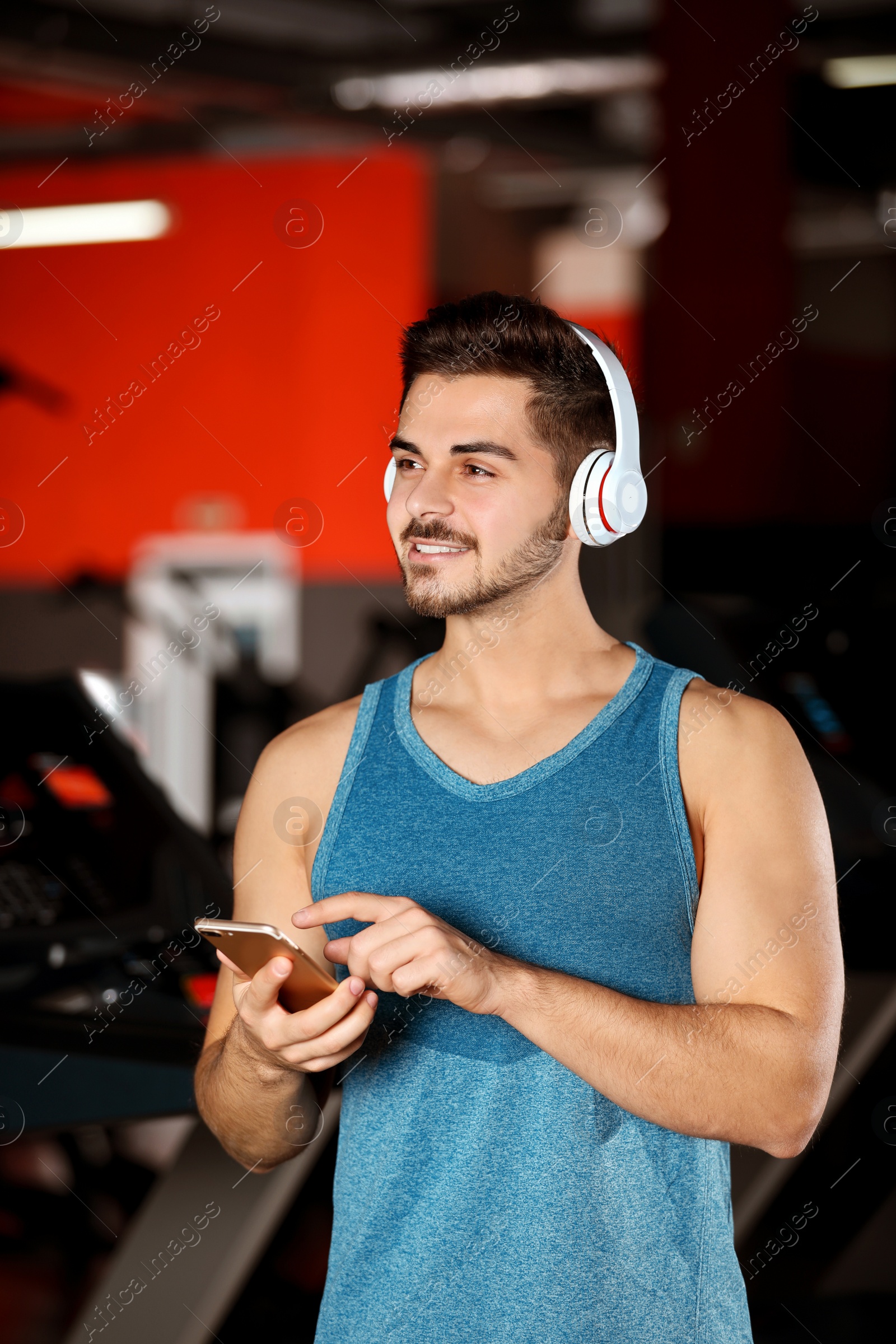 Photo of Young man with headphones listening to music on mobile device at gym