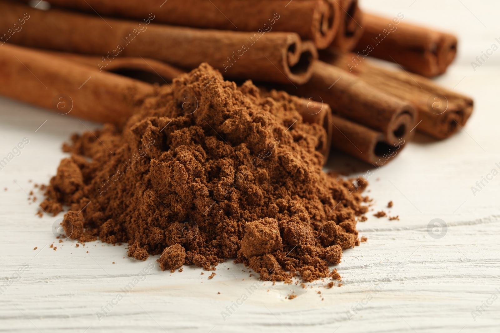 Photo of Aromatic cinnamon powder and sticks on white wooden table, closeup