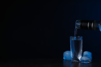 Photo of Pouring vodka from bottle in glass and ice cubes on black background. Space for text