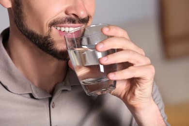 Photo of Happy man drinking water indoors, closeup. Refreshing drink
