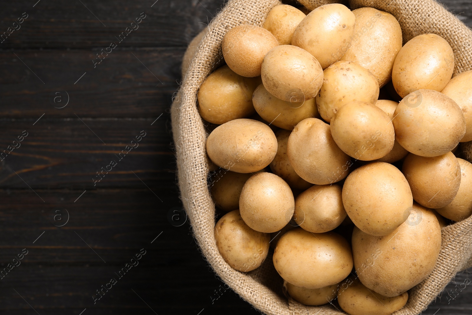 Photo of Raw fresh organic potatoes on black wooden background, top view. Space for text