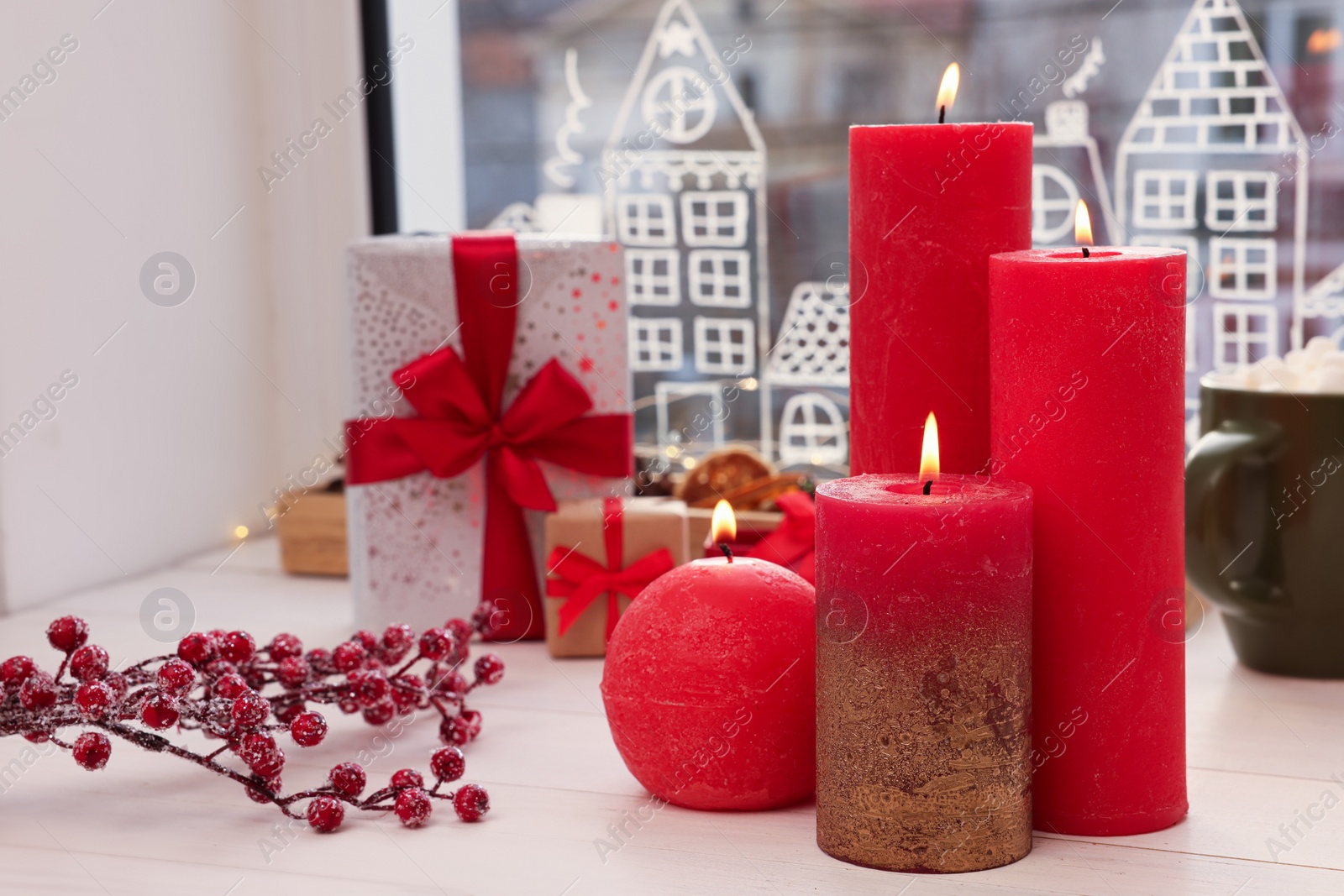 Photo of Beautiful burning candles with Christmas decor on white wooden table near window