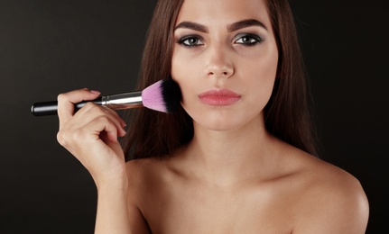 Photo of Portrait of beautiful woman applying stylish makeup with brush on dark background