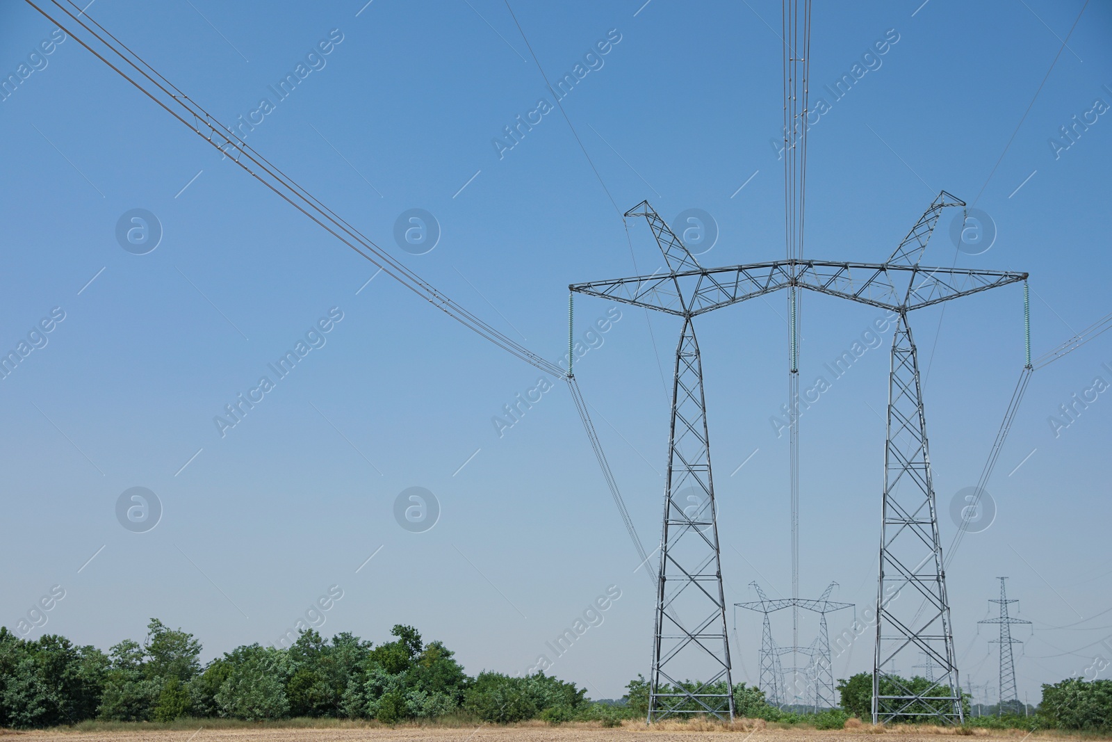 Photo of High voltage towers with electricity transmission power lines in field on sunny day