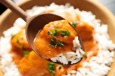 Photo of Spoon with tasty butter chicken over bowl of meal, closeup