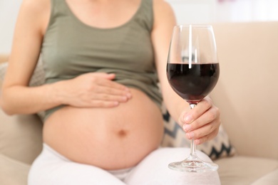 Photo of Pregnant woman with glass of red wine at home, space for text. Alcohol addiction