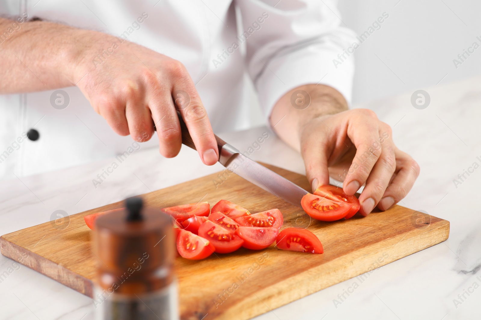 Photo of Chef cutting tomatoes at marble table in kitchen, closeup