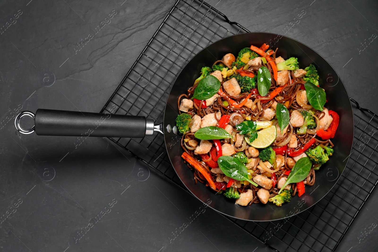 Photo of Stir-fry. Tasty noodles with meat and vegetables in wok on grey textured table, top view