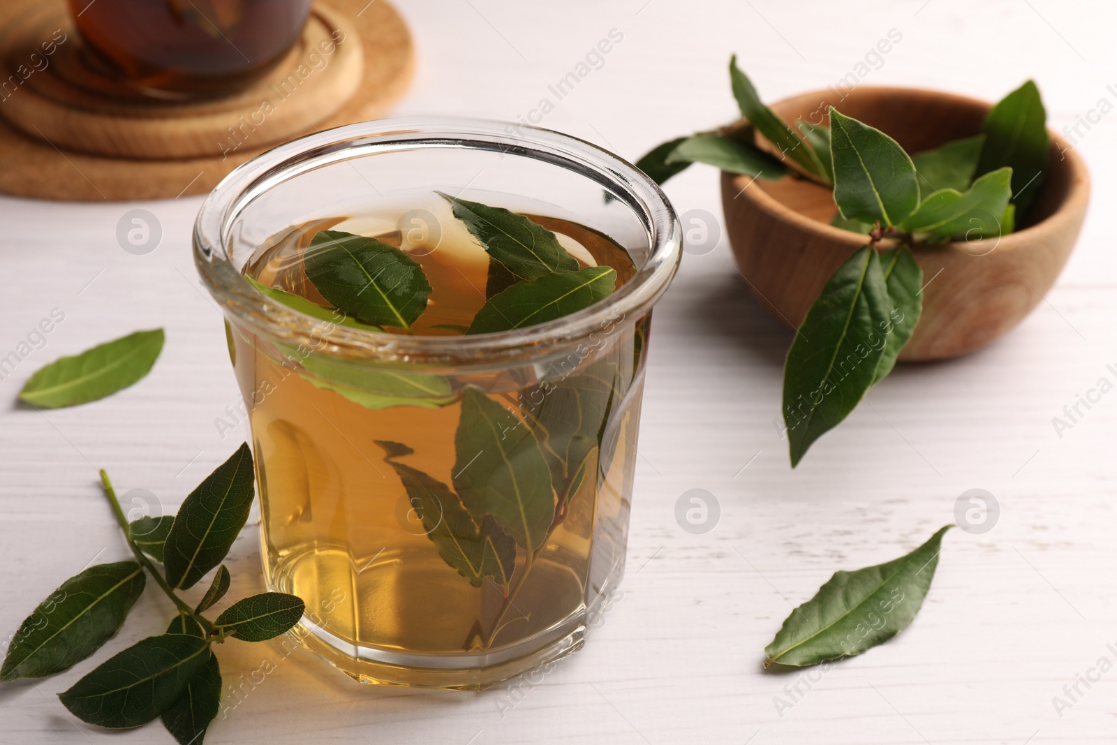 Photo of Cup of freshly brewed tea with bay leaves on white wooden table, closeup