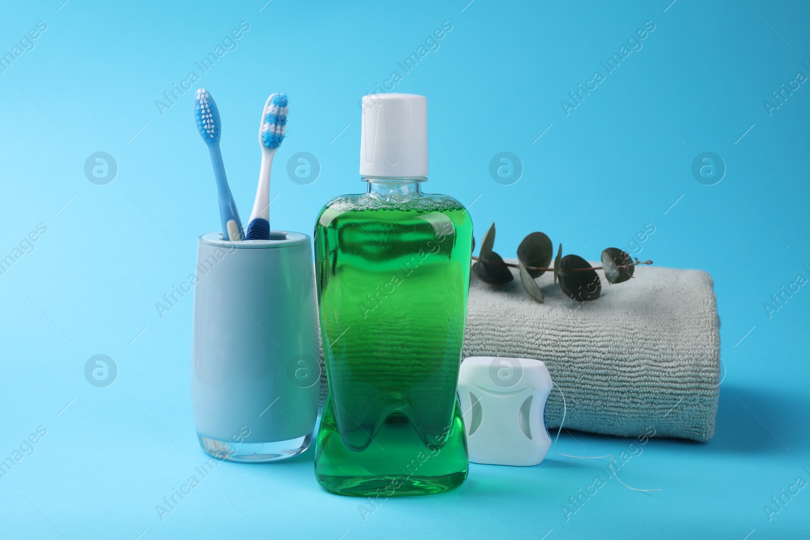 Photo of Fresh mouthwash in bottle, dental floss and toothbrushes on light blue background