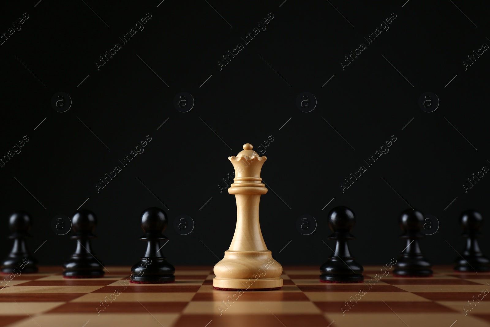 Photo of White queen among black pawns on wooden chess board against dark background