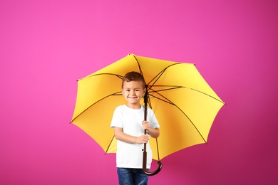 Photo of Little boy with yellow umbrella on color background