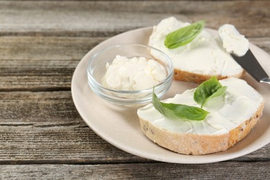 Photo of Delicious sandwiches with cream cheese and basil leaves on wooden table. Space for text