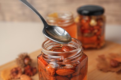 Photo of Spoon of honey above glass jar with nuts, closeup